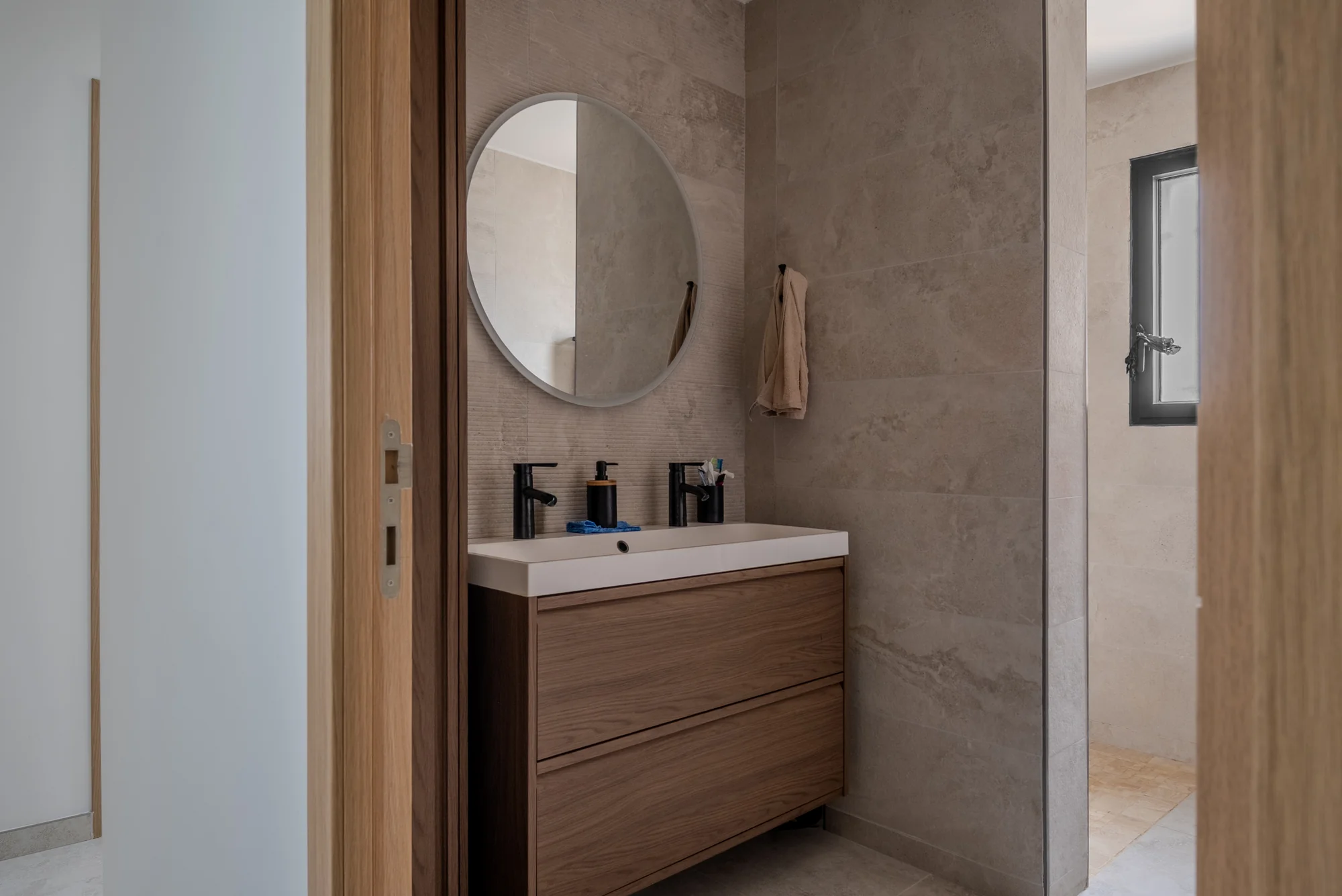 Salle d'eau avec meuble vasque en bois et miroir rond, photographie immobilière